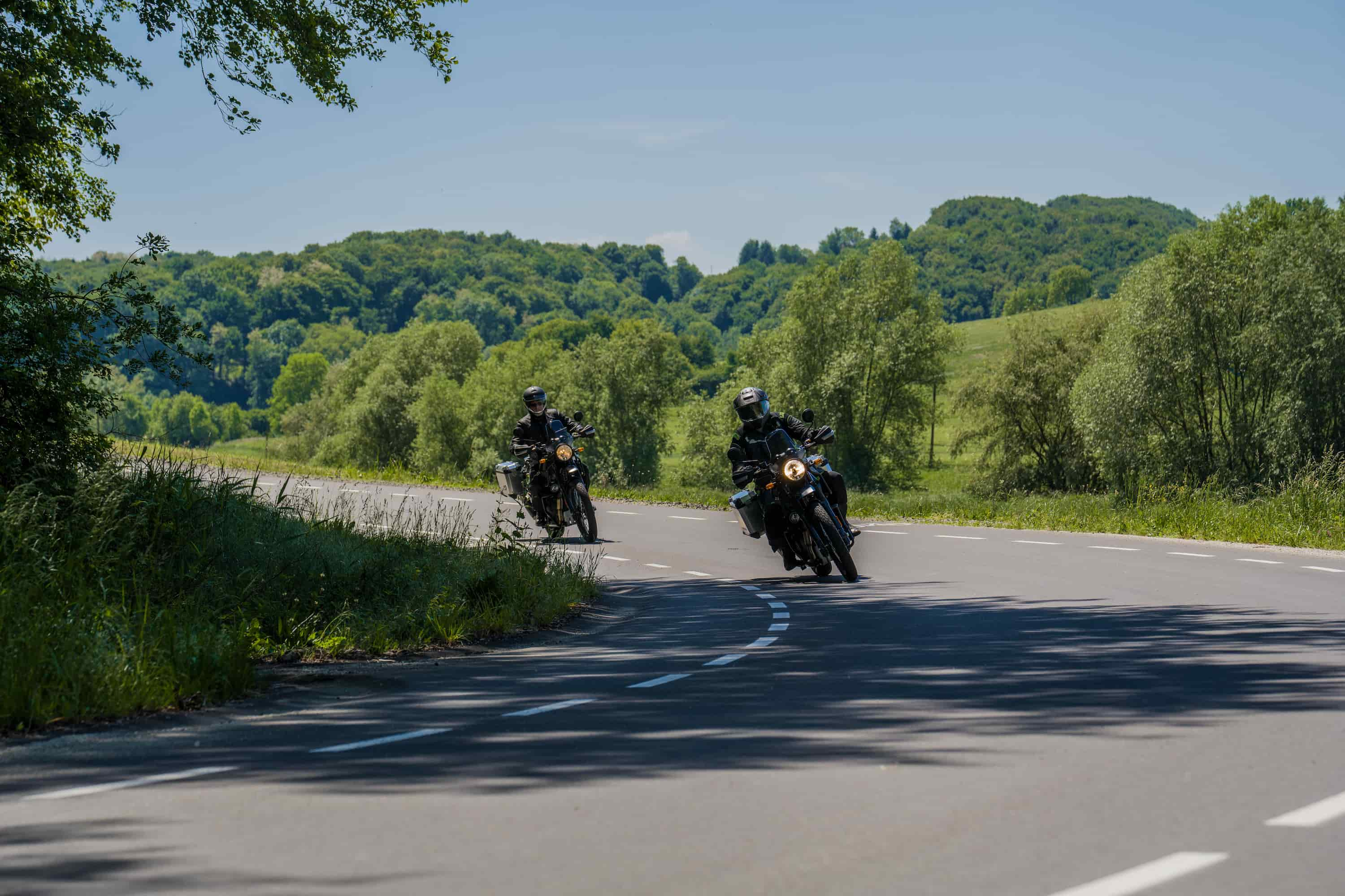 2 men driving royal enfield motorcycles around a tight bend